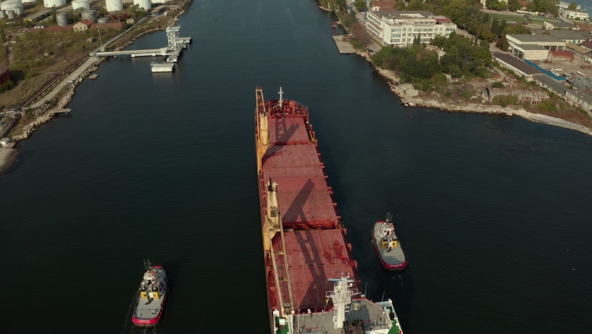 Aerial view of cargo ship calling into the port for repair under the guide of tugboats.