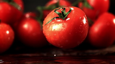 Super slow motion fresh tomato falls on the table with splashes of water. Filmed at 1000 fps.On a wooden background.