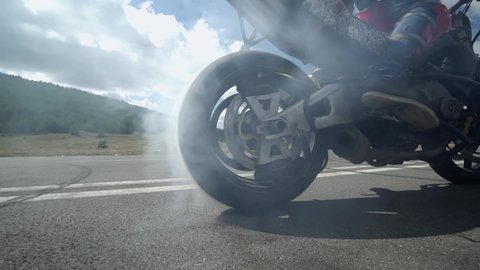 Motorcycle wheel burning tires and smoking on race track, stunt man doing tricks on motorcycle in slow motion