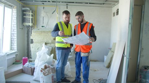 Male builders discussing draft during renovation works