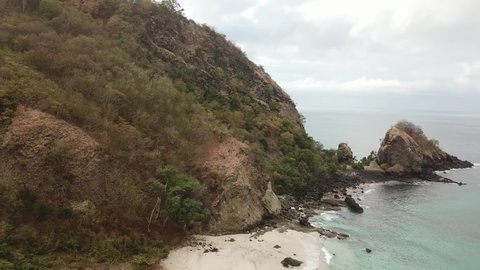 A panoramic view on Koka Beach. Hidden gem of Flores, Indonesia. Beach is gently washed by waves. Steep hills going straight into the sea. Few boulders popping out of the sea. Serenity and calmness
