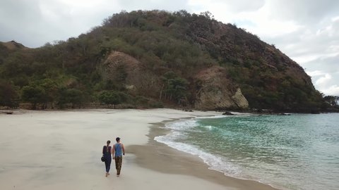 A man running along idyllic Koka Beach. Hidden gem of Flores, Indonesia. Couple is enjoying their romantic escape. Waves gently washing the shore. There are hills in the back. Adventure and discovery

