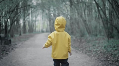 Small child in a yellow raincoat with a hood is walking in the dark scary forest towards the highway. The concept of lost children and scary dreams and fairy tales