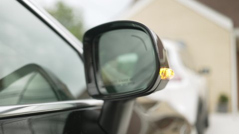 A closeup view of a luxury car's side rear view mirror opening then retracting. Front view.  	