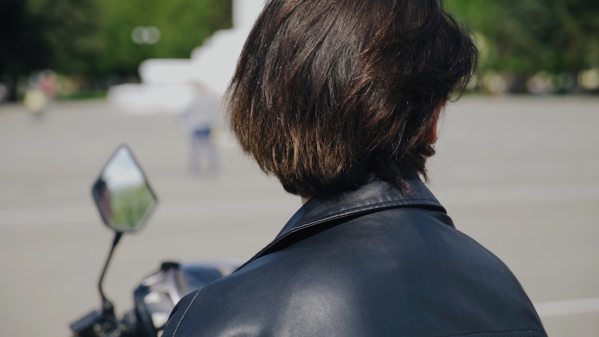 Beautiful young biker girl sitting on a motorcycle. In her ear is an earring in the form of a cross. Close-up shooting