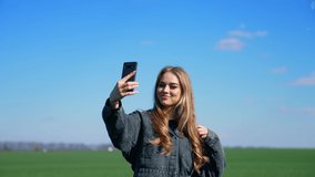 Attractive girl doing video call in nature. Young blogger woman talking on a phone camera while walking on a green meadow in a sunny day.