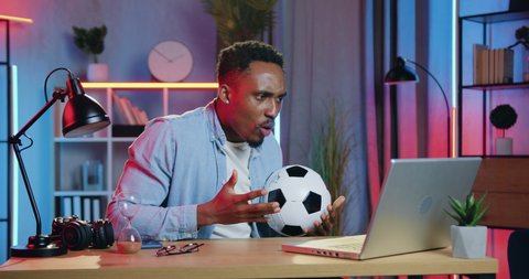 Likable excited funny young male black-skinned football fan watching football match online on computer and is dissatisfied as his favourite team lost the game