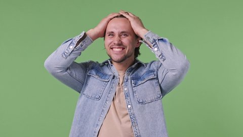 Joyful jubilant surprised shocked young man 20s years old in denim shirt say wow omg what spread hands doing winner gesture put hands on face screech isolated on pastel green color background studio