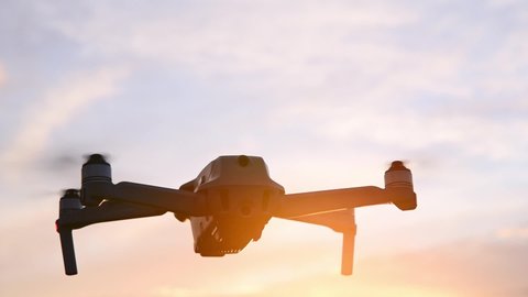 Drone flies against the bright evening sun during sunset golden hour.