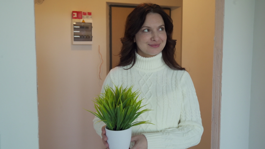 Happy woman owner moving in new flat, smiling lady with pretty face holding flower pot enter new apartment, mortgage, relocation and welcome. Home construction concept.