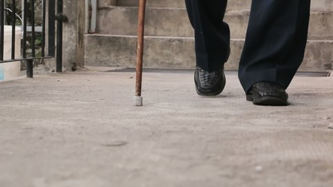 The old man walks with a cane. The old man's legs as he walks with a cane