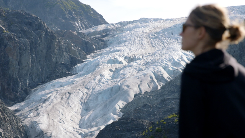 Female Standing in Front of Alaskan Glacier, Slow Motion Changing Depth of Focus Shot. Global Warming and Climate Change Concept