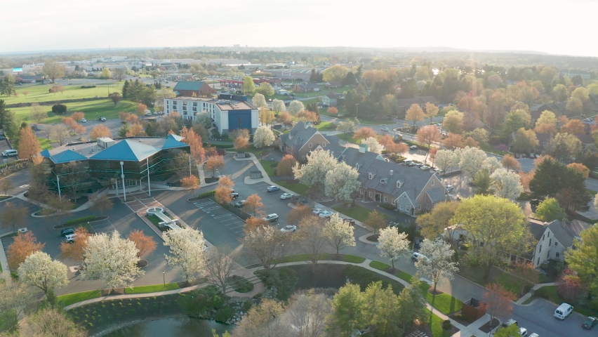 Business park with office buildings. Descending aerial on spring trees in colorful bloom. Magic golden hour sunlight.