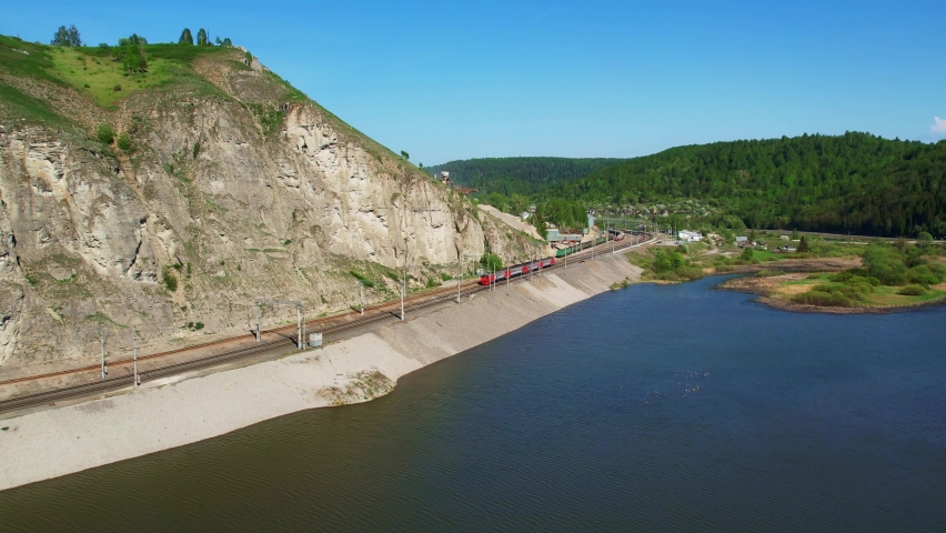 The train rides on the railway past picturesque places. Rocks and a river.
