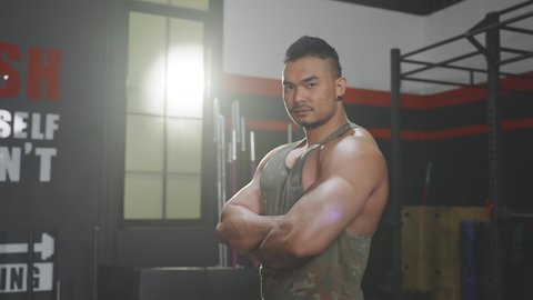Asian attractive Active Fitness sportman trainer workout exercise to maintain muscle and biceps for health. Bodybuilder athlete male stand with arm crossed and smile, look at camera in stadium or gym.