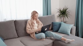 Blonde girl sitting on the couch, working on a laptop. Remote work online