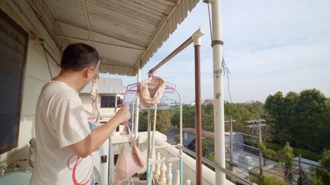 Asian man hanging up undergarments to dry on his apartment balcony - slow motion