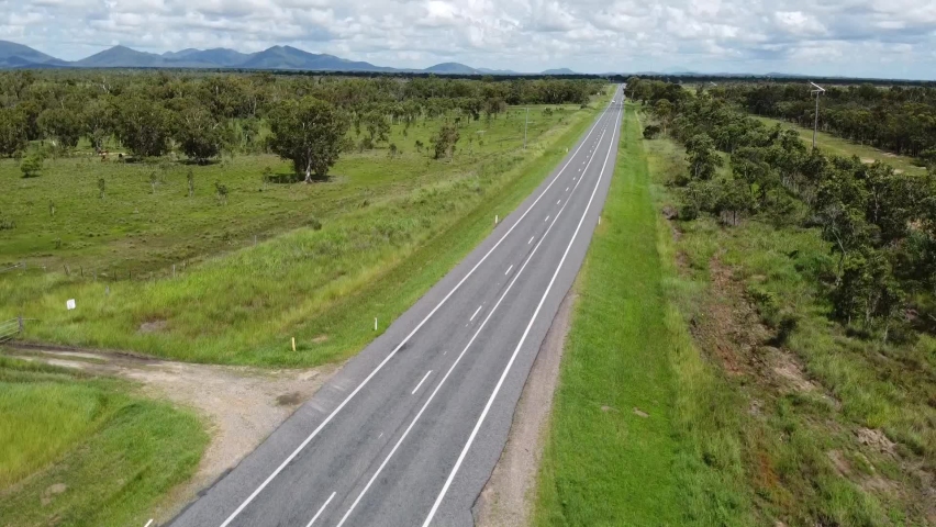 Aerial drone shot of green land and straight road going through Queensland in Australia