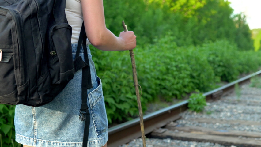 A girl with a backpack and a stick in her hand walks along the sleepers. Travel on railroad tracks. Old train track 4k