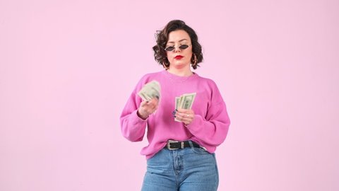 Stylish avarice woman counts a wad dollar money isolated on pink background. Easy money.