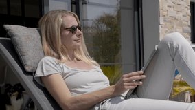 Blond woman at home relaxing in long chair on sunny day