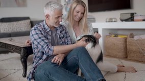 Happy couple with dog relaxing at home, sitting on carpet
