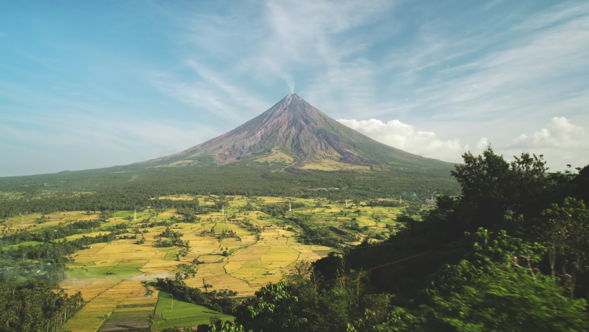 Volcano peak eruption at tropic farmlands aerial. Nobody nature landscape at summer. Hillside green grass valley at river. Countryside tourist attraction of Mayon Mount, Legazpi town, Philippines