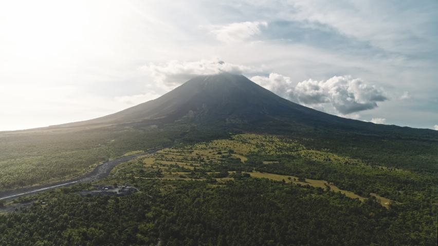 Aerial panorama of volcano erupt at sunrise. Nobody nature landscape. Sun rising over green exotic plants, grasses valley at mountain hills with tropic river. Legazpi town, Mayon, Philippines, Asia