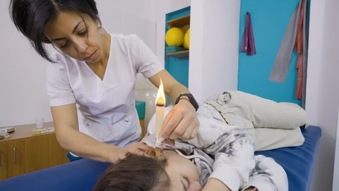 Medium shot of a therapist performing an ear wax ral treatment on a patient using candling.