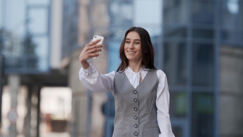 Cheerful young woman in a business suit takes a selfie video on a smartphone