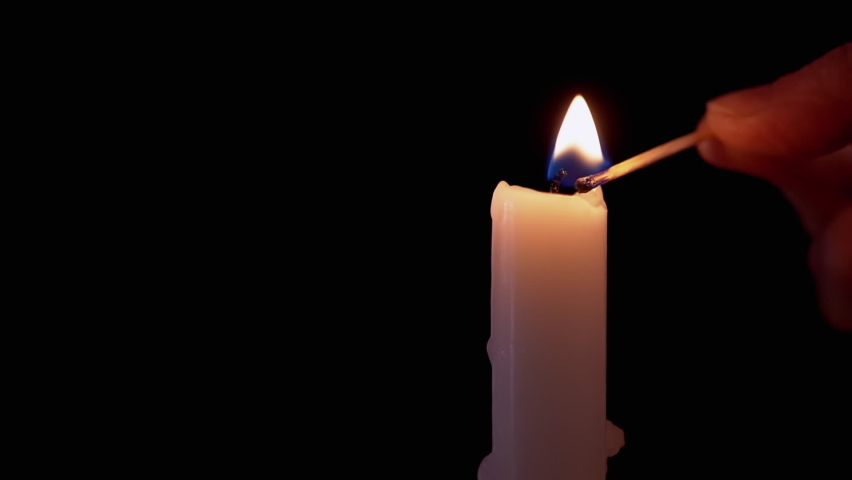 Female Hand Lights Paraffin Candle using a Match on a Black Background. Bright flame, fire, ignition in a dark room. White candle with yellow fire. Concept of memory, ritual, celebration. Slow motion. | Shutterstock HD Video #1072949120