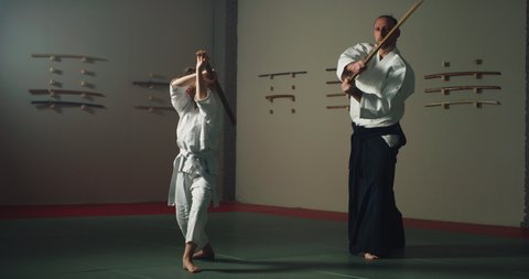 Cinematic shot of fighter master and his pupil practicing with wooden sword Aikido training in modern Japanese martial arts school. Concept of sports, recreation, defense, religious beliefs.