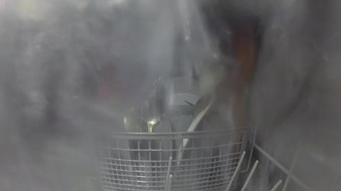 Inside the dishwasher. The process of washing dishes. Water jets spray and wash plates, mugs, forks, spoons and other utensils. The nozzle mechanism rotates. Digital camera inside the dishwasher.