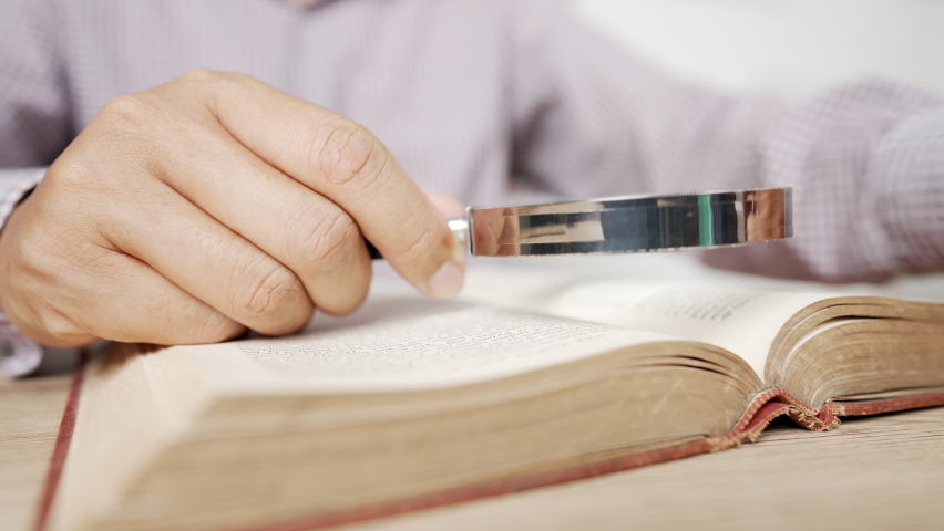 Close-up Hand Man using magnifying glass for reading the book,Knowledge accumulation and history concept.