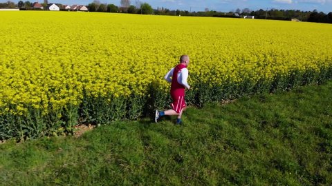 young father sportsman jogging near flower field. happy lifestyle concept. Young happy male running on a green meadow with yellow colza flower field on the background. with free copy space