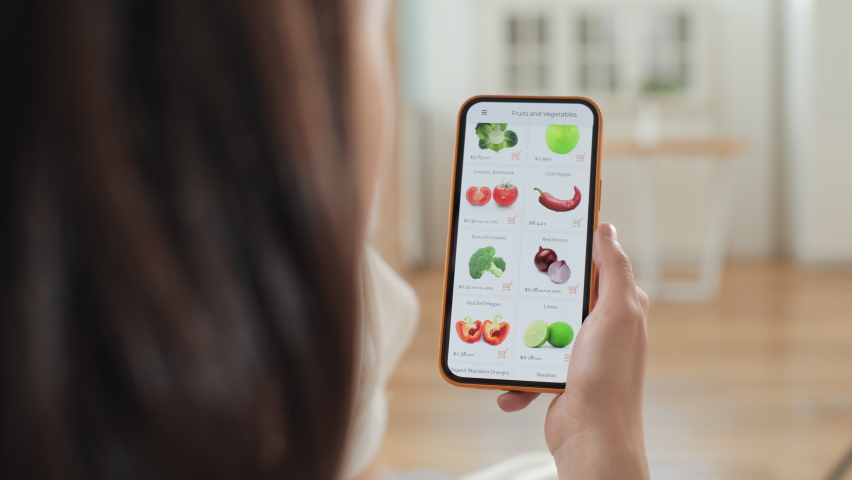 Hand holds mobile phone and scrolls up web page of grocery store. Use online payment to buy healthy organic food in market application closeup. Leisure of beautiful woman relaxing indoors of cozy home Royalty-Free Stock Footage #1072958480
