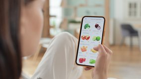 Hand holds mobile phone and scrolls up web page of grocery store. Use online payment to buy healthy organic food in market application closeup. Leisure of beautiful woman relaxing indoors of cozy home - Powered by Shutterstock - Get 15% off with code: PIKWIZARD15