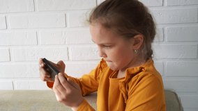 schoolgirl girl in a yellow longstyle, playing with her smartphone in an enlarged manner, turning it horizontally. The child plays a computer game - driving a car or catching