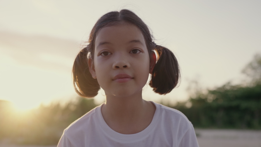 Happy Asian little girl playing to camera  in sunlight or sunset, Portrait of child smile enjoy playing soap bubbles and cheeky expression, Close up of face woman