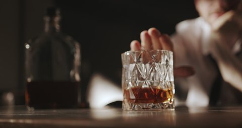 The man pushes the glass of whiskey away from him with a confident movement of his hand. With this gesture, he indicates that he will no longer drink alcohol. 