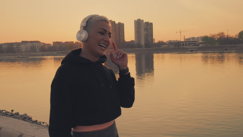 Young athlete woman singin and listening to the music over headphones outdoors.