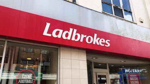 Birkenhead, UK, May 22nd 2021: Ladbrokes logo name and facade, open for business for gaming, gambling and Horse racing betting. Static shot of main entrance red and white sign.