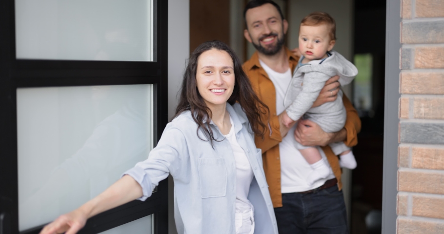 Young and cheerful family with a kid opens door and invites to their house