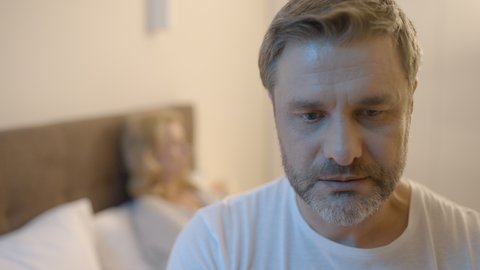 Stressed middle-aged man sitting in bed, suffering low libido, unhappy marriage