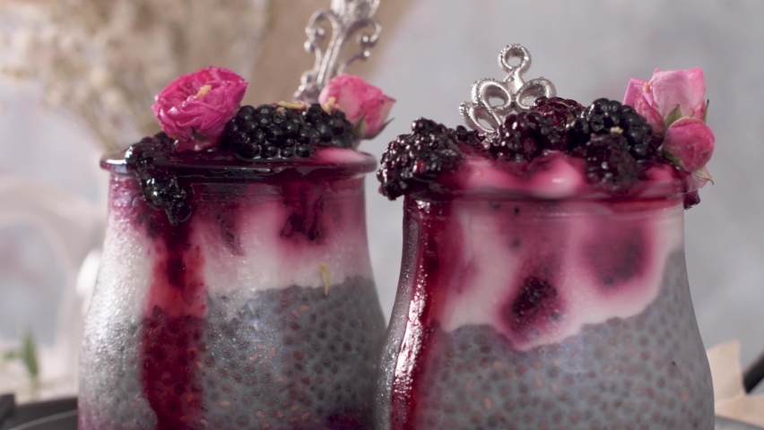 Layered chia pudding topped with fresh blackberries, berry coulis, and delicate pink rosebuds. The scene features soft natural lighting and rustic textures.