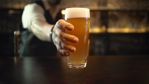 Bartender serving customers in pub, puts pint of beer. Mug of unfiltered beer.