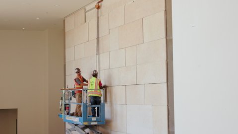 San Diego, California, USA - October 7, 2019: Stonemasons lifting and installing heavy limestone tiles to finish a wall in a new theater lobby.
