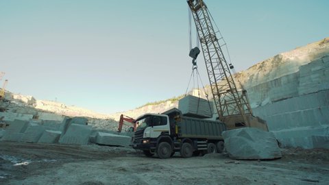 Mining Industry. A Crane is loading a Heavy Truck with granite stone. A slab of Granite is Being Lowered inside of the Truck. Dumper Truck is used for transporting materials at a Quarry. Slow-motion.