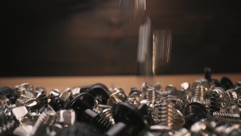 Pile of computer screws, more small screws dropping as camera pull back with macro probe lens, slow motion
