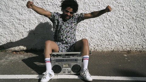Young Afro Latin man having fun dancing while listening music with headphones and vintage boombox during summer vacations